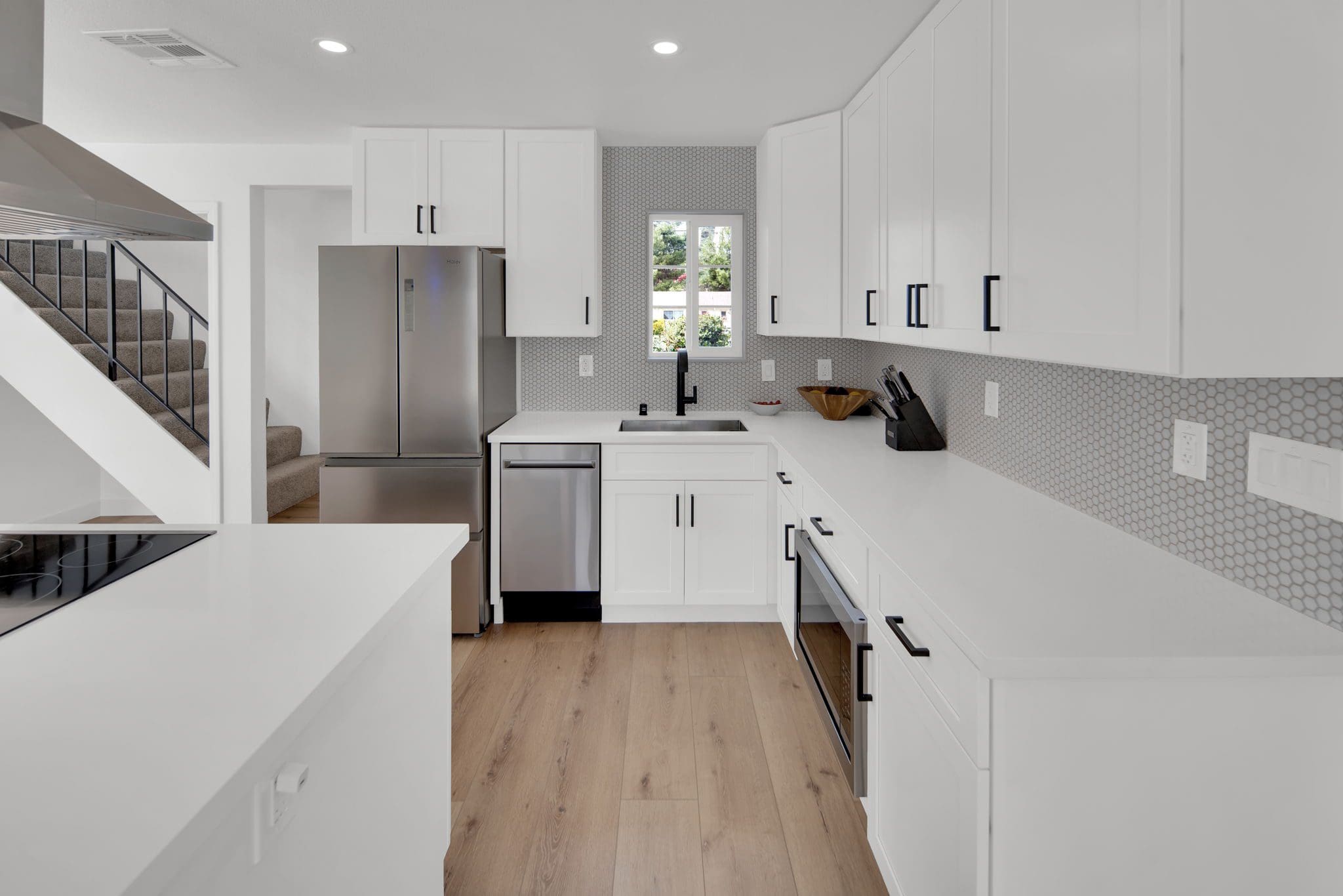 Modern kitchen with white cabinets, stainless steel appliances, and wood floor.