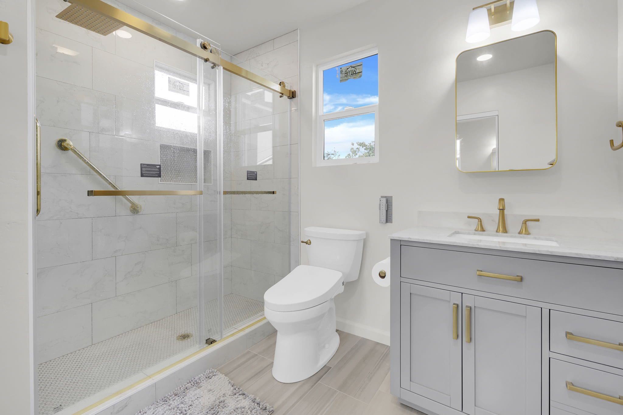 Modern bathroom with walk-in shower, toilet, and vanity with gold fixtures.