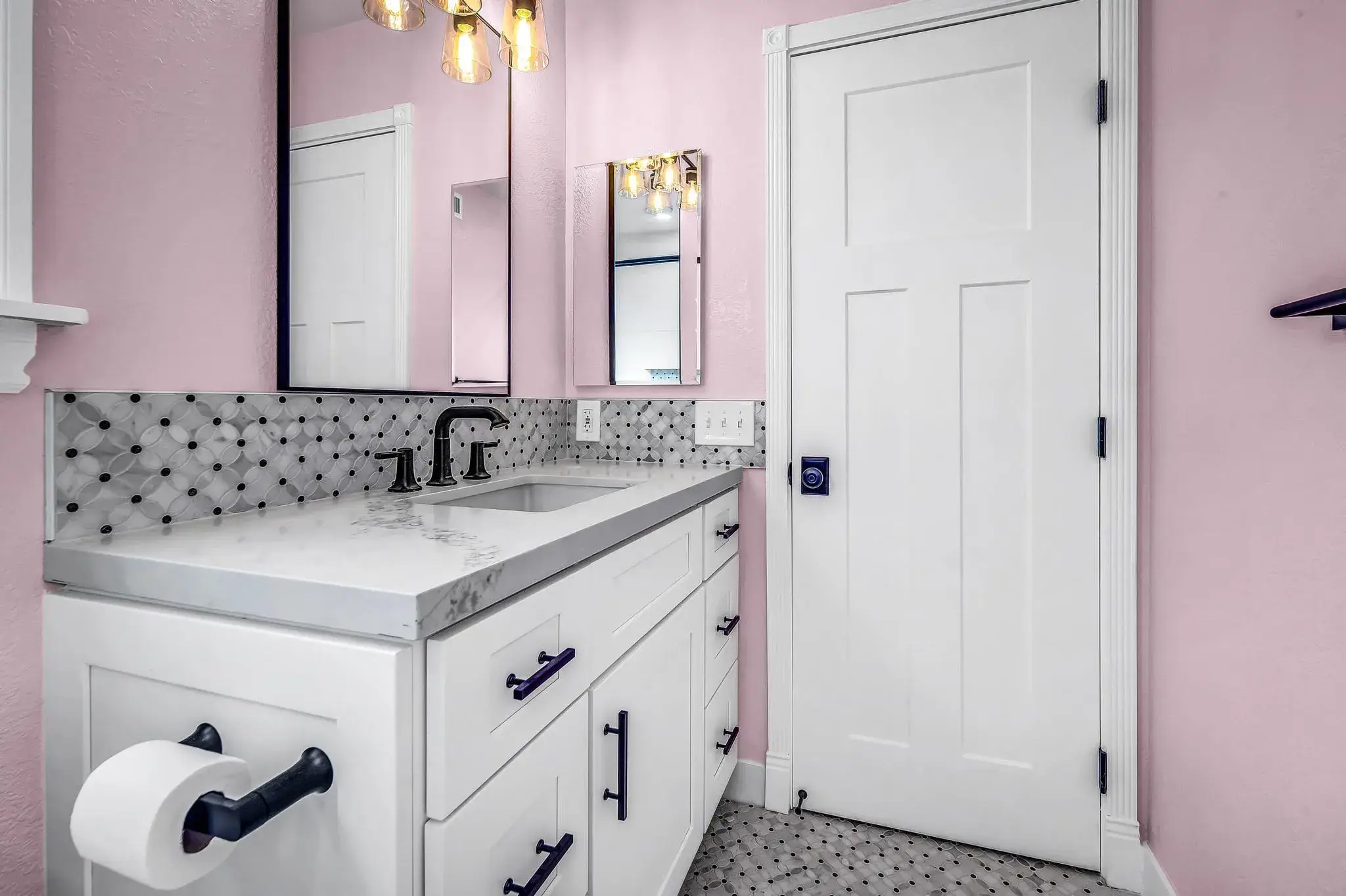 Bathroom with pink walls, white vanity, and black and white tiled floor.