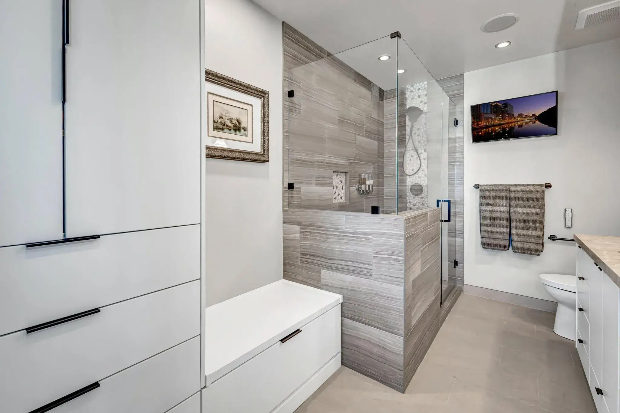 Modern bathroom with walk-in shower, white cabinets, and a wall-mounted TV.