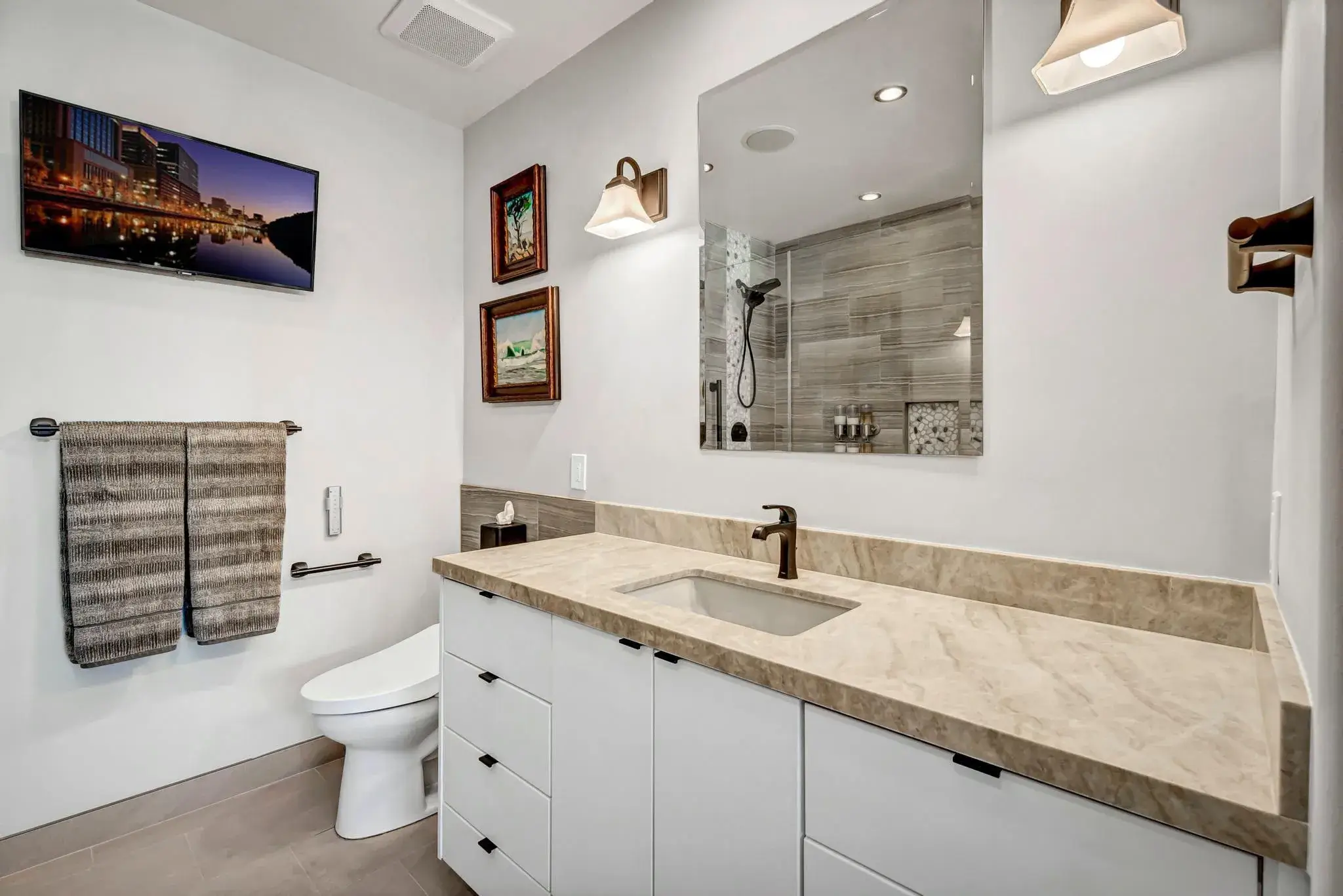 Modern bathroom with a large vanity, mirror, toilet, and mounted TV.