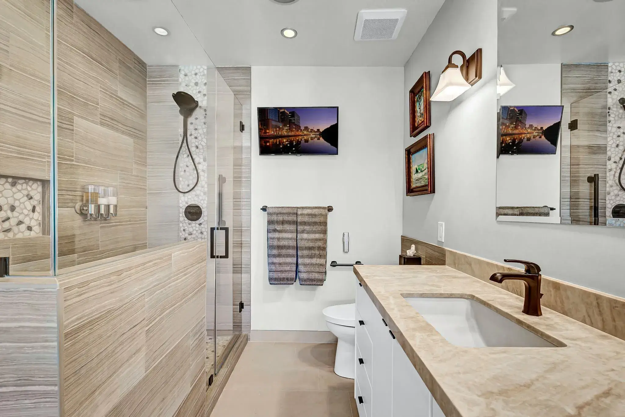 Modern bathroom with walk-in shower, vanity, toilet, and wall-mounted TV.
