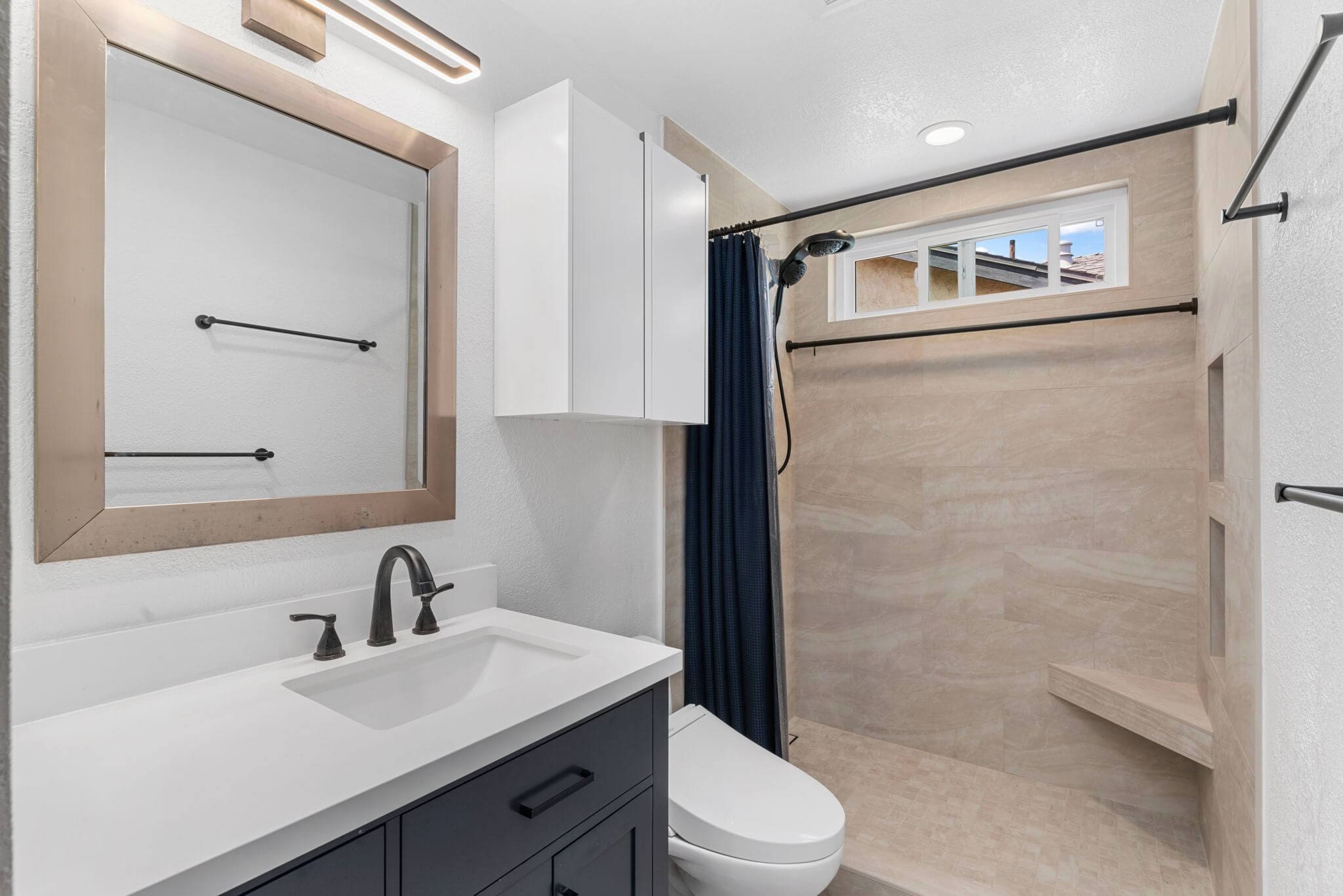 Modern bathroom with dark vanity, white sink, large mirror, and walk-in shower.