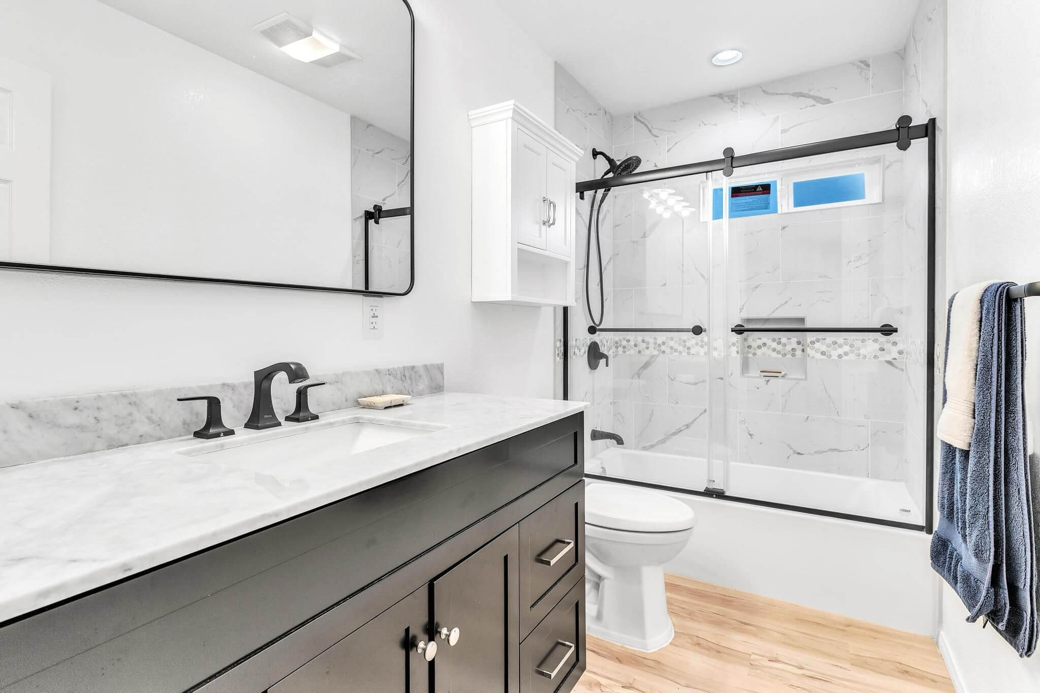 Modern bathroom with dark vanity, white marble counter, and tiled shower.