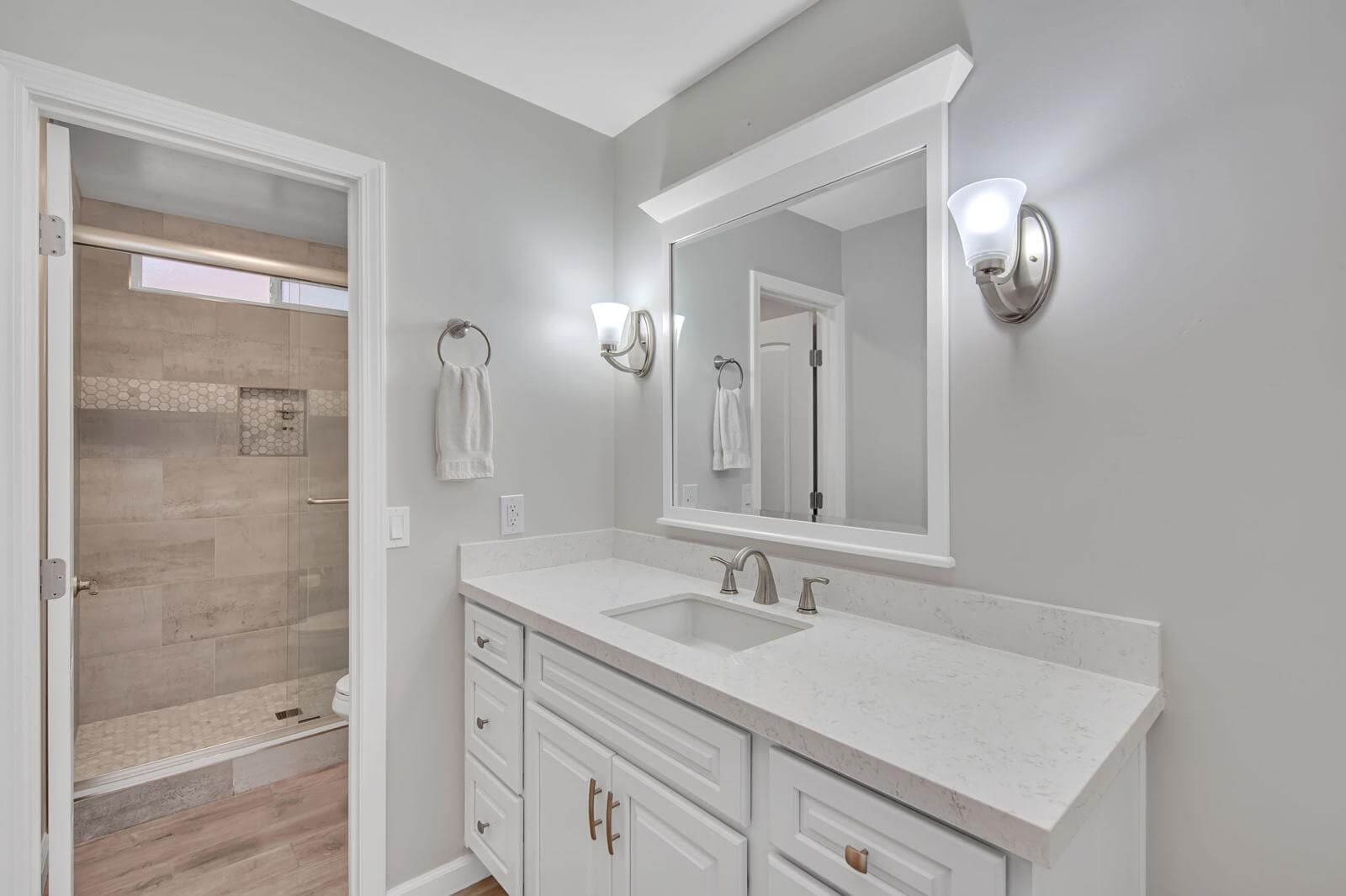 Modern bathroom with white vanity, mirror, and shower with light gray walls.