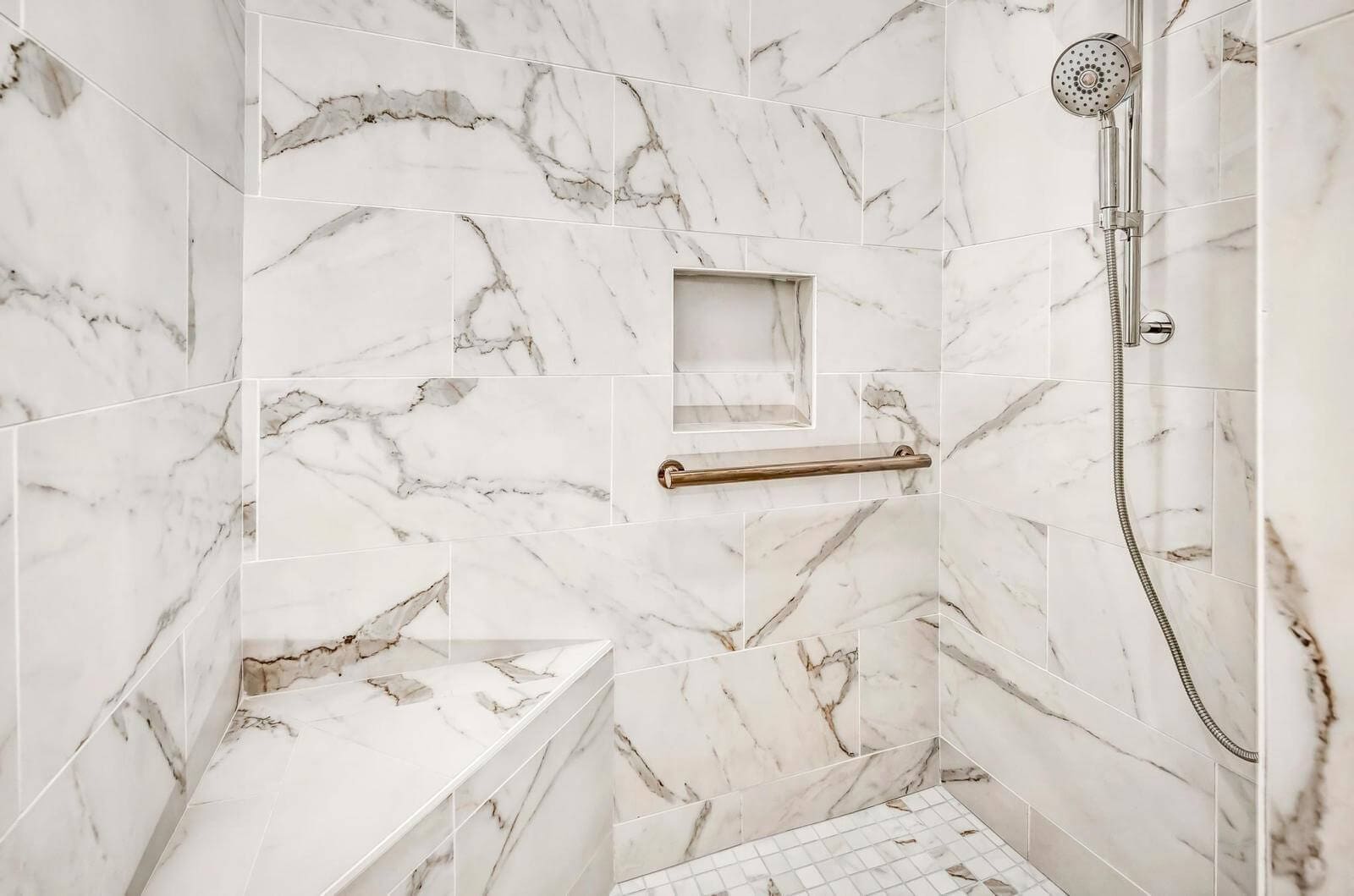 A white marble shower with a built-in bench and grab bar.