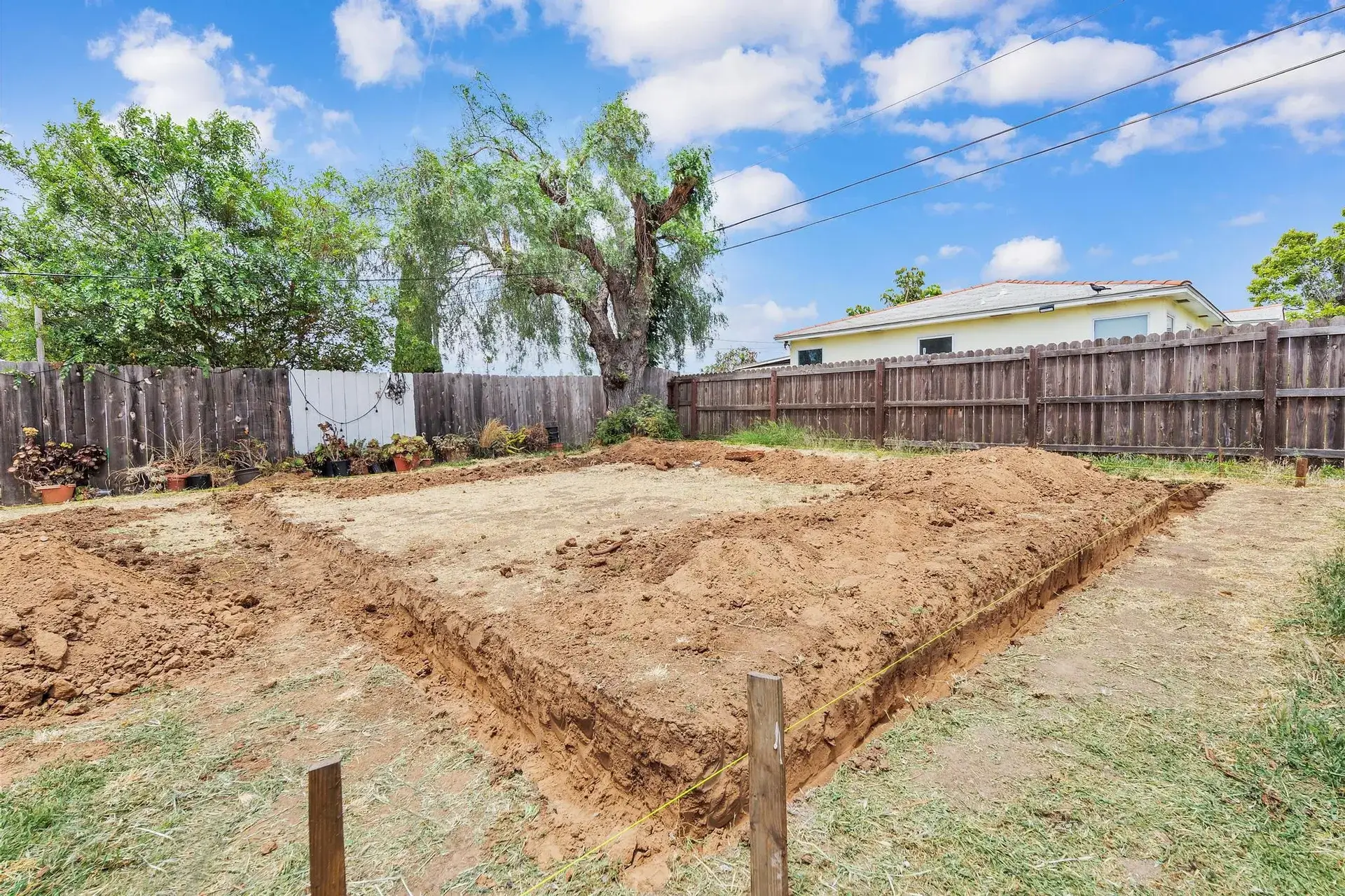 Excavated backyard with dirt piles and wooden fence under a blue sky