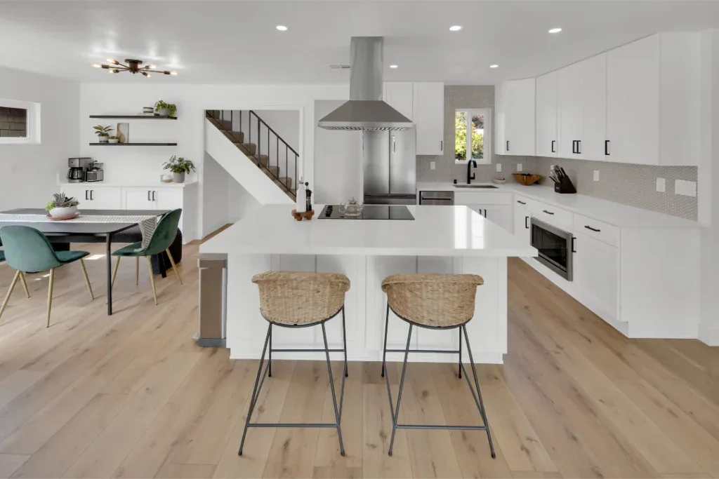 Modern white kitchen with island, two bar stools, and dining area.