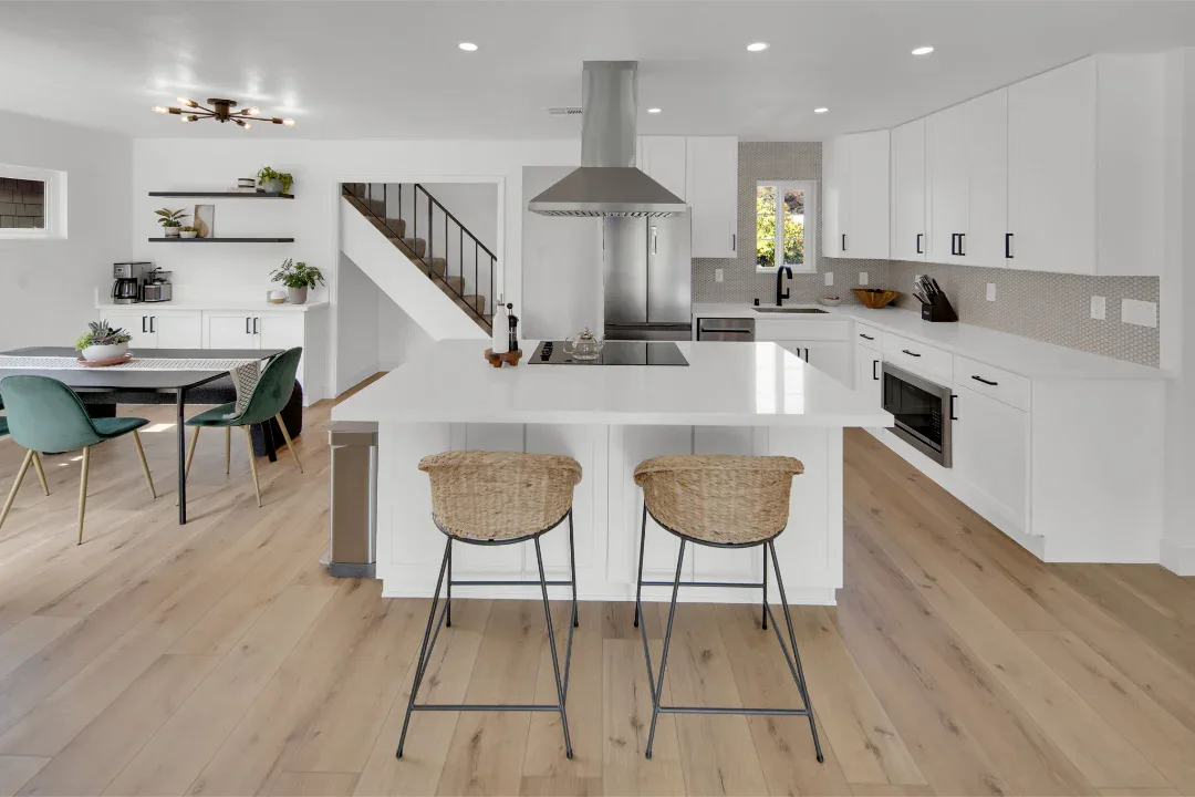 Modern white kitchen with island, two bar stools, and dining area.