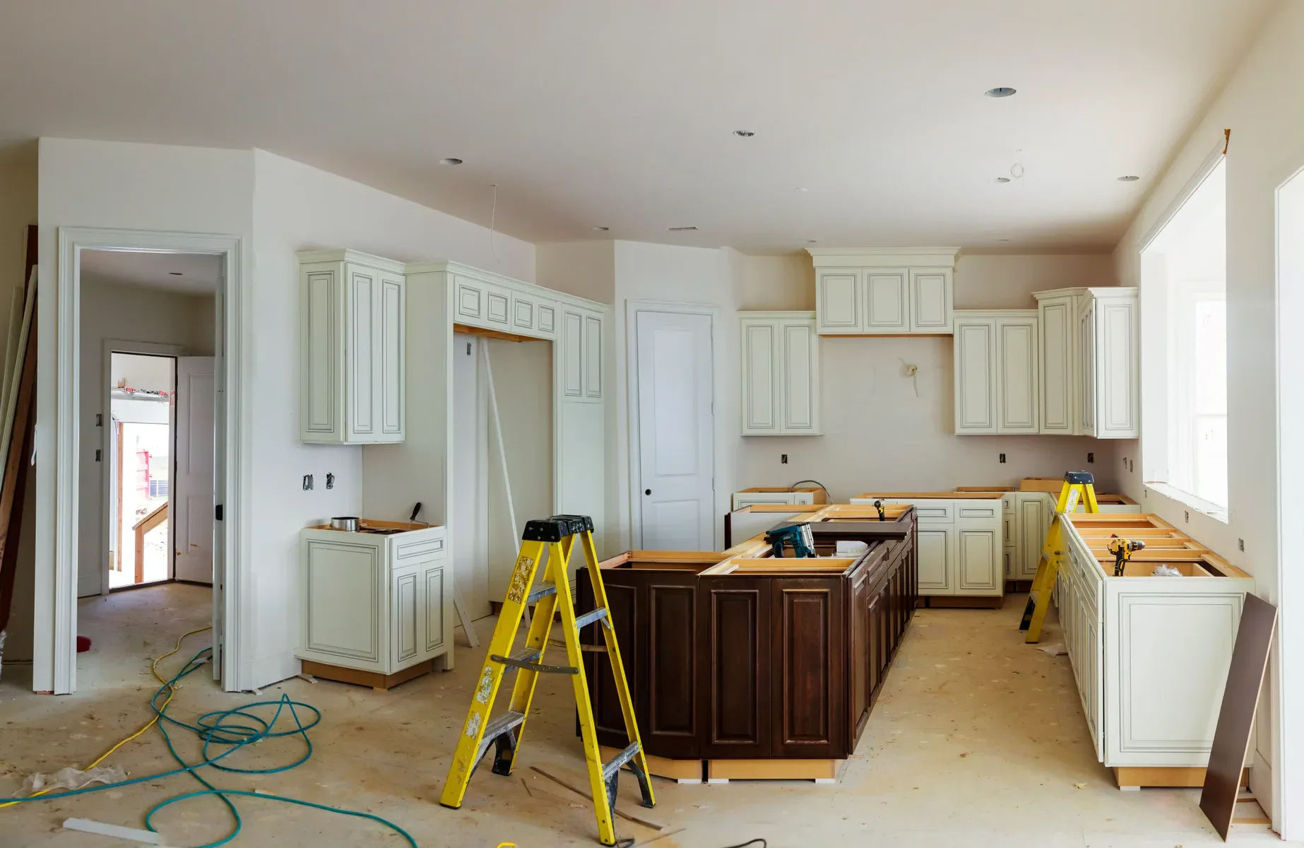 Unfinished kitchen with white cabinets, dark brown island, and yellow ladder.