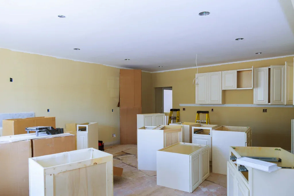 Kitchen under construction with light yellow walls and new white cabinets.