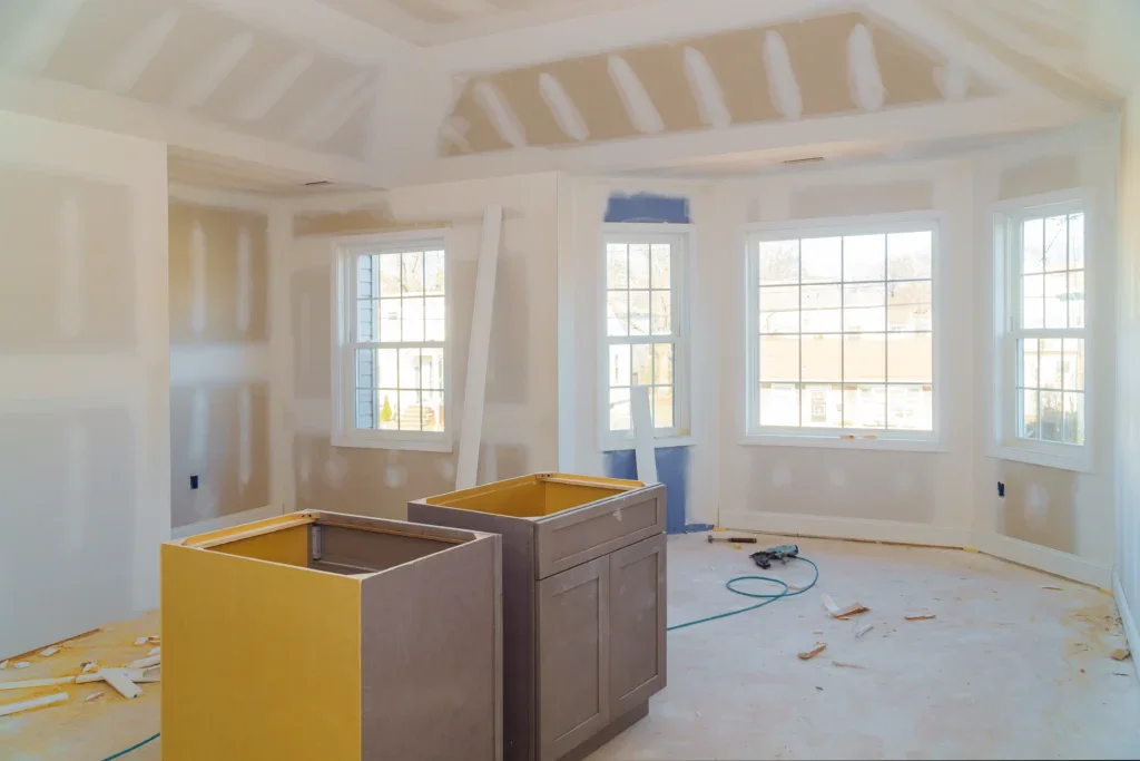 Interior room under construction with new drywall, windows, and cabinets.