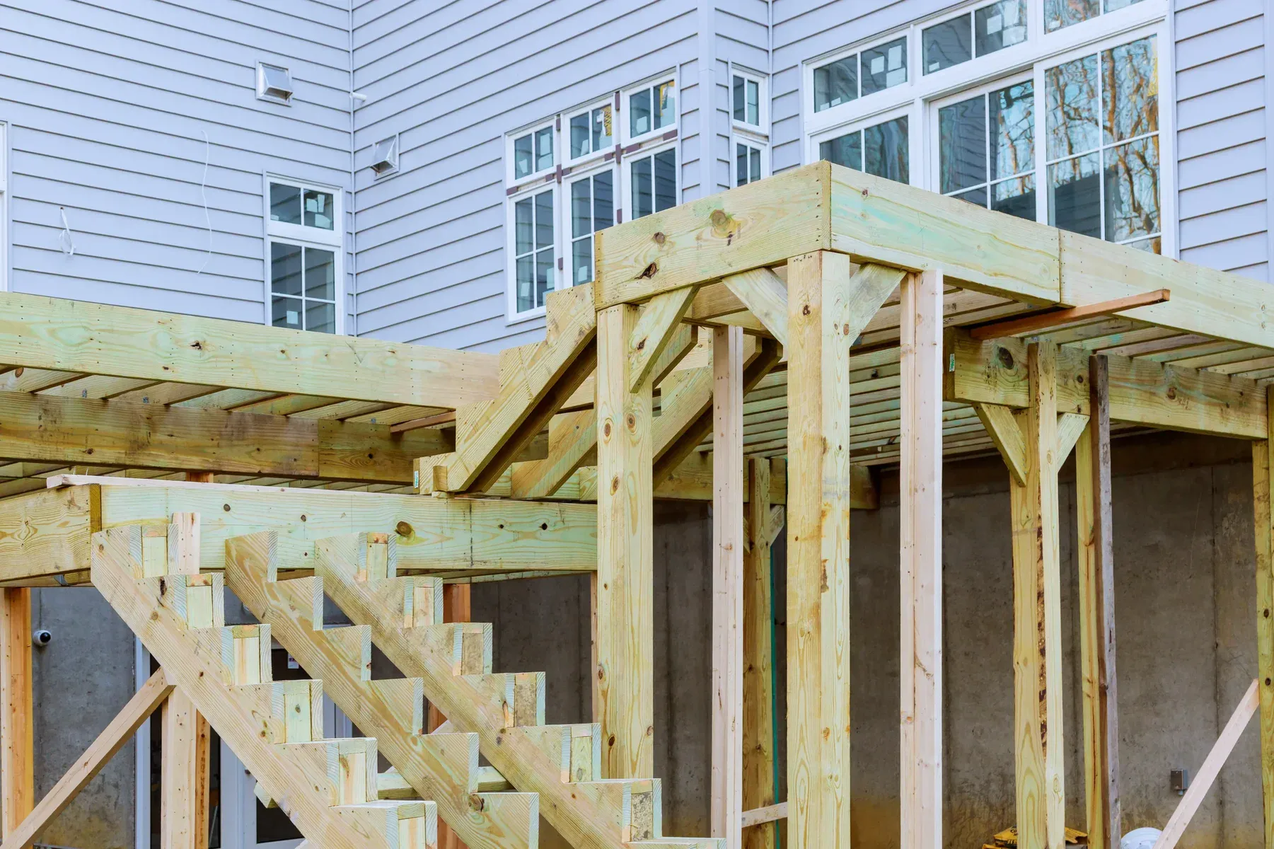 New wooden deck frame and stairs under construction next to a house