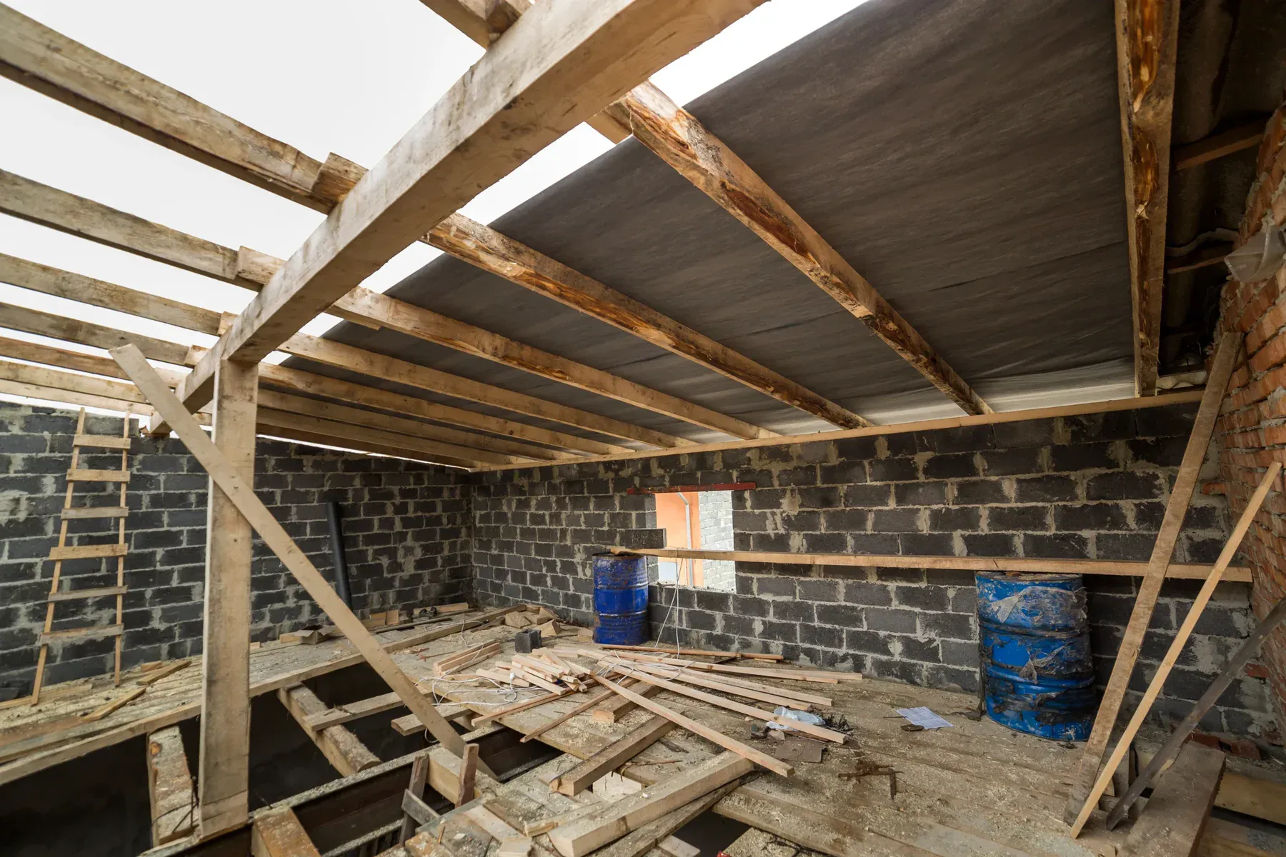 Interior of a house under construction with exposed wooden beams and brick walls.