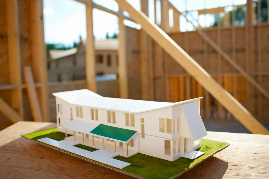 Architectural model of a white house with green roof detail on a wooden surface.