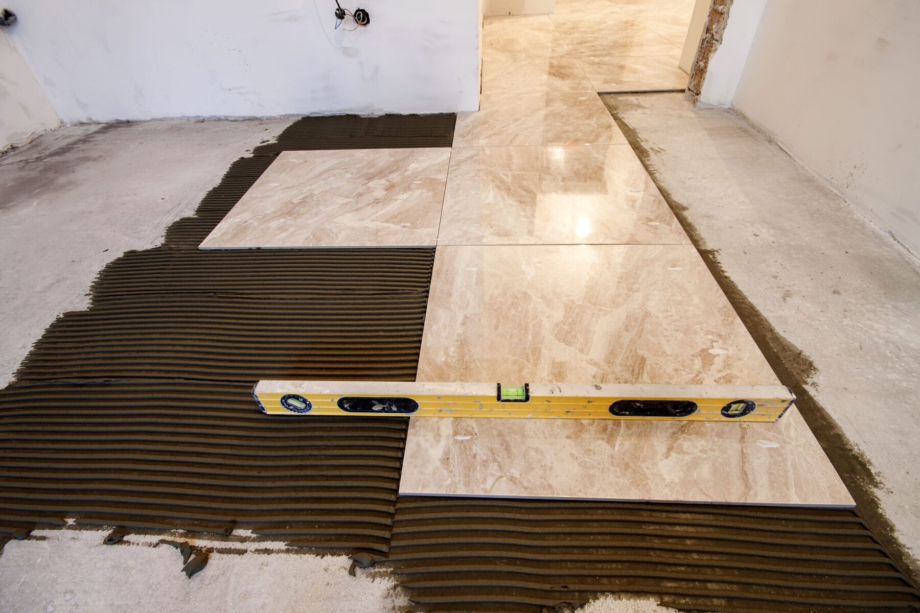 Ceramic tiles being laid on a floor with adhesive and a level