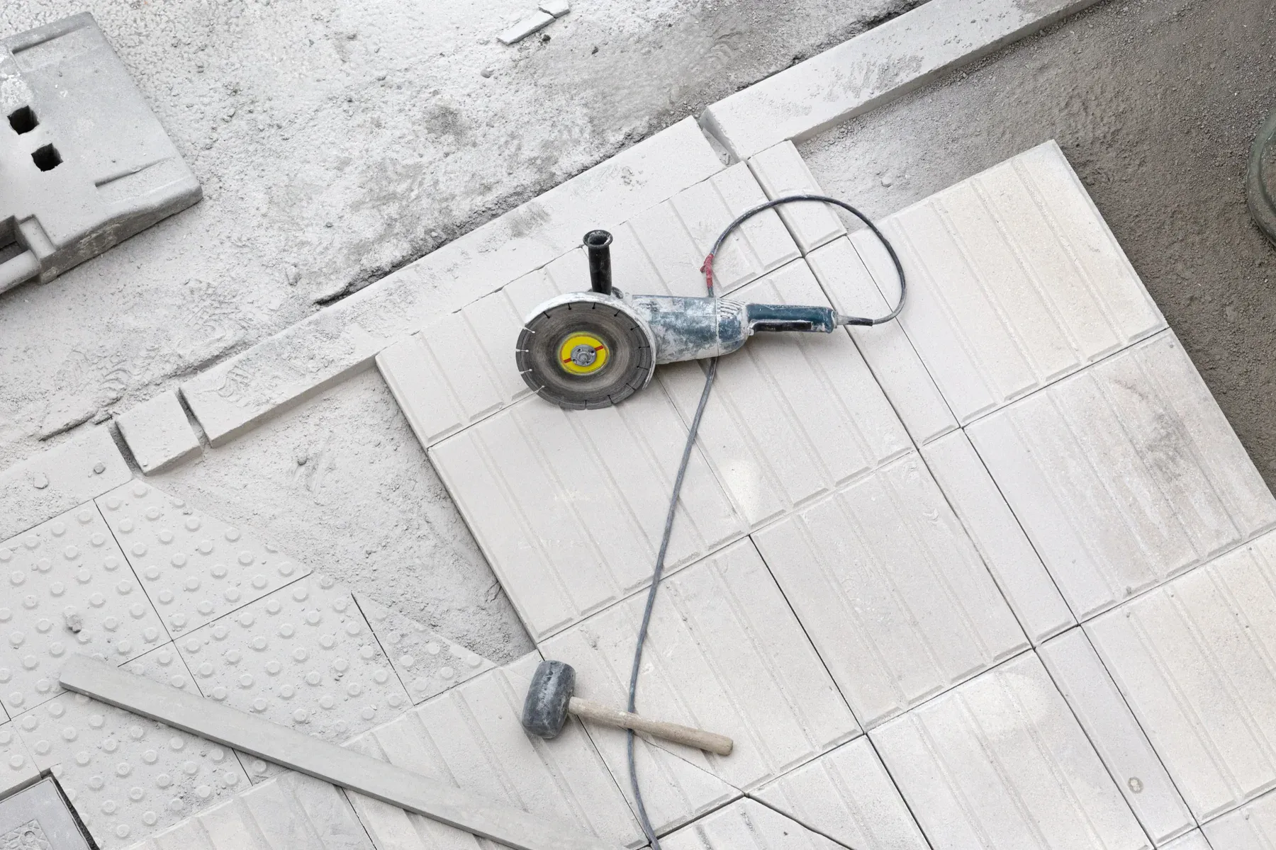 Overhead view of an angle grinder and hammer on light-colored paving stones.