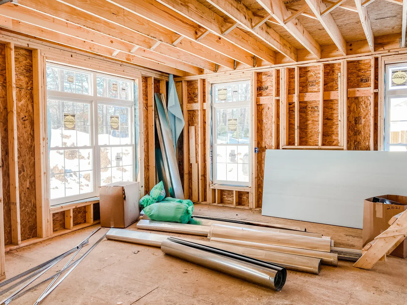 Interior of a house under construction with exposed wooden framing and windows.
