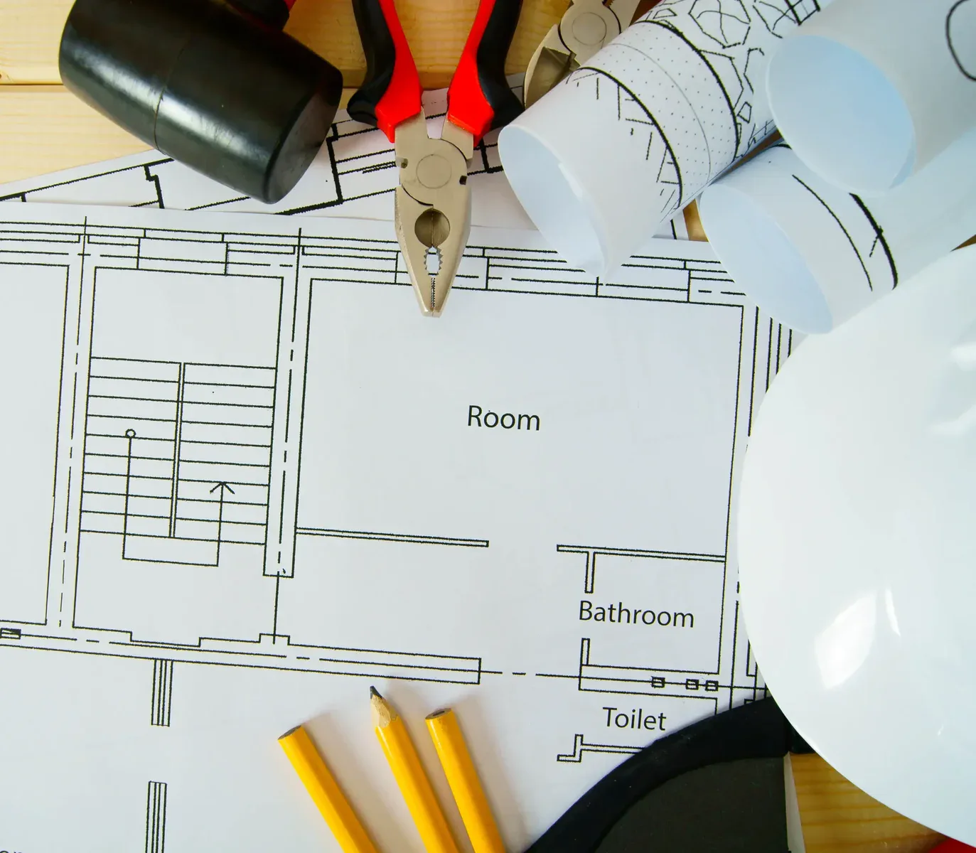 Architectural blueprints with tools, pencils, and a hard hat on a wooden surface.