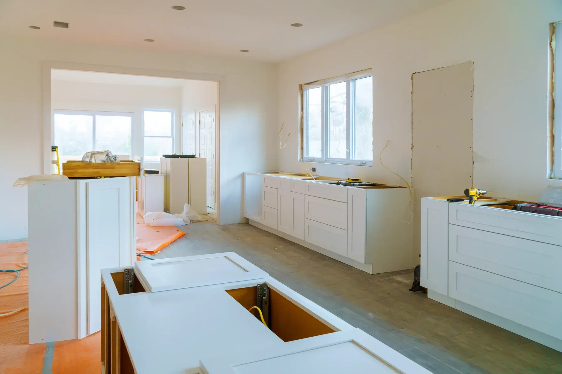 Kitchen under construction with white cabinets and windows