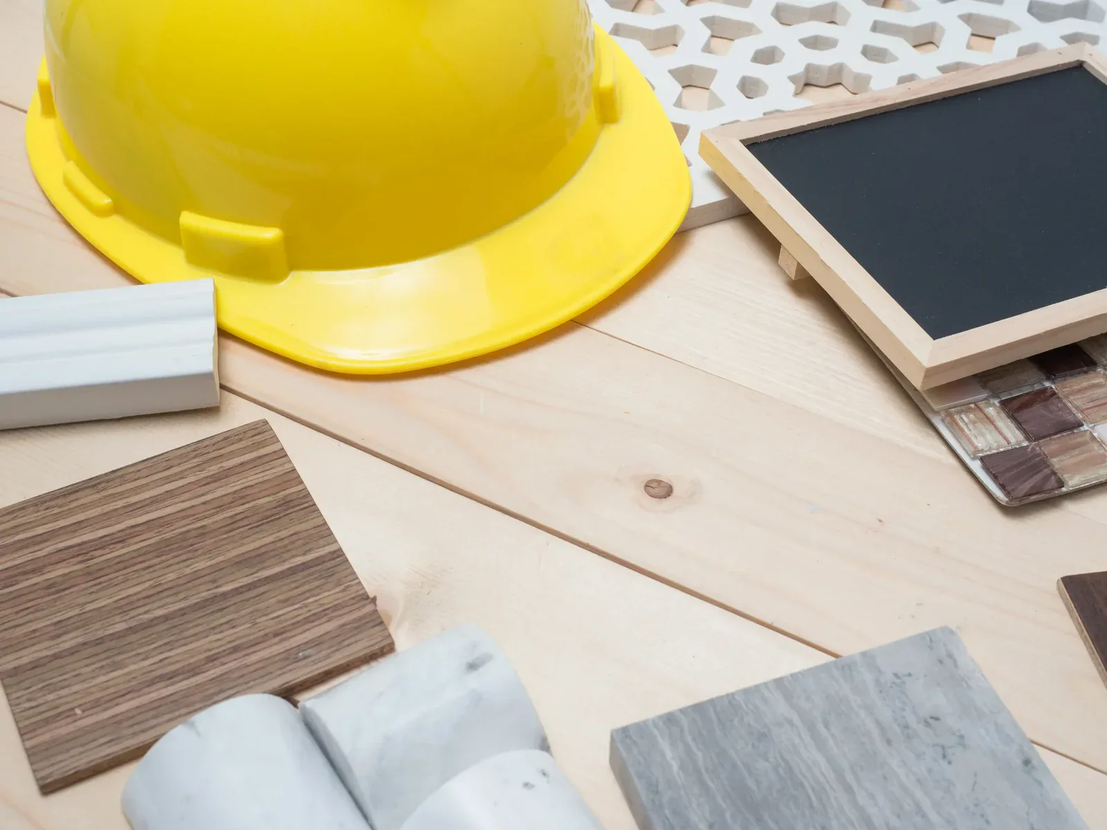 Yellow hard hat, wood, tile, and marble samples on a light wooden surface.