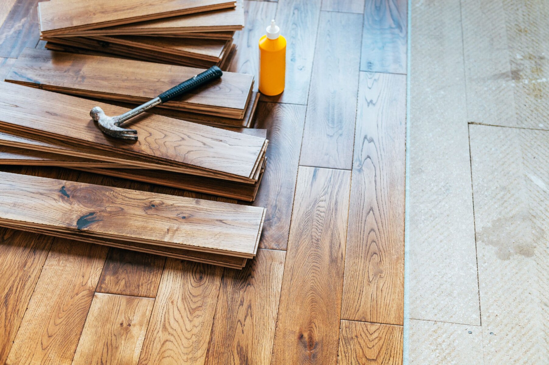 Hammer, wood glue, and wood flooring planks on a wooden floor