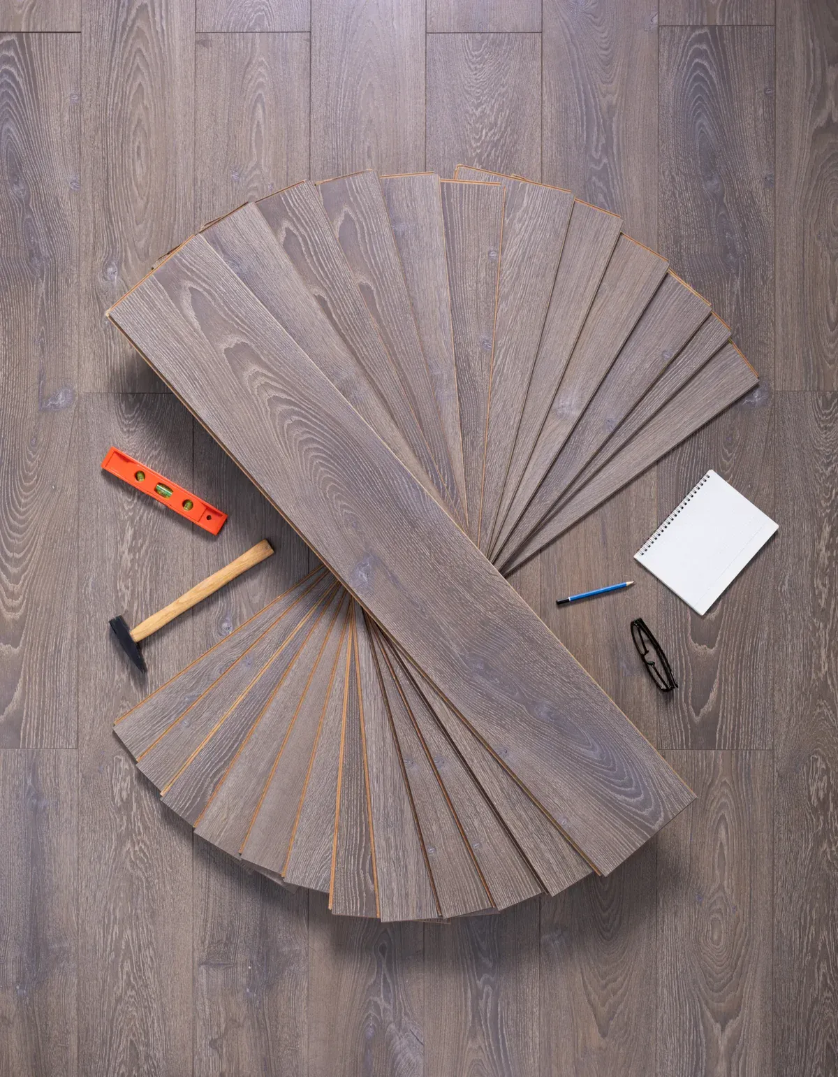 Laminate flooring planks arranged in a fan shape with tools on a wooden floor.