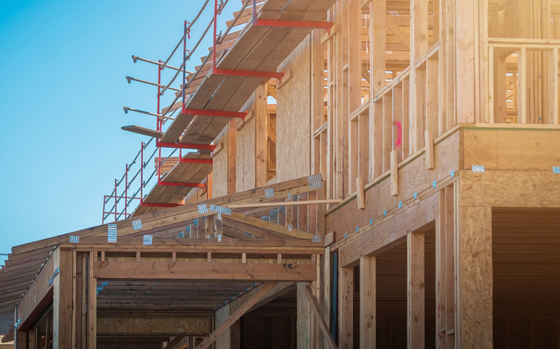 New house construction with wooden framing and scaffolding against a clear sky