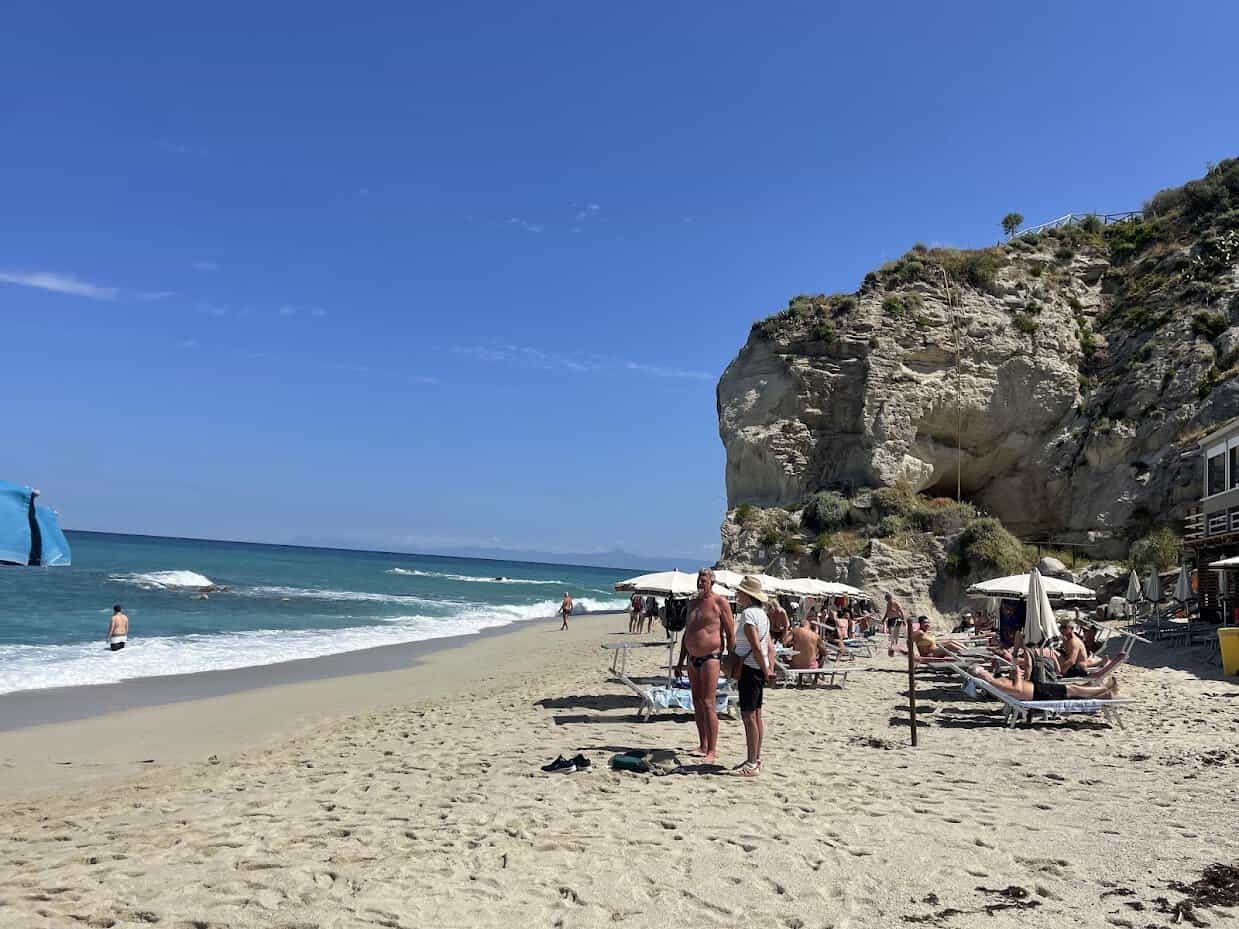 Beautiful Linguata beach in Tropeawith cliffs, sunbathers, and clear blue sky.
