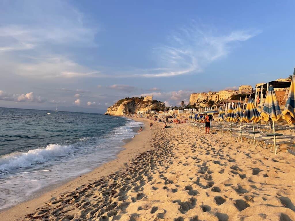 Scenic view of Mare grande beach with umbrellas and cliffs at sunset.