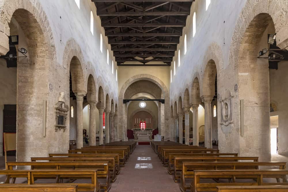 Inside the Santa Maria Cathedral Gerace in Calabria, with original stone arches and marble columns, and timber benches.