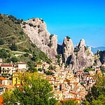 historic mountain village of Castelmezzano, one of southern italy destinations, with jagged rocky peaks behind the village on a blue sky day