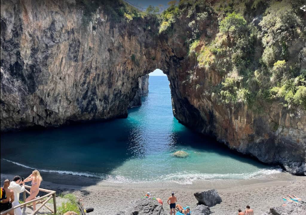 Scenic natural arch on Calabria beach with turquoise waters and visitors.
