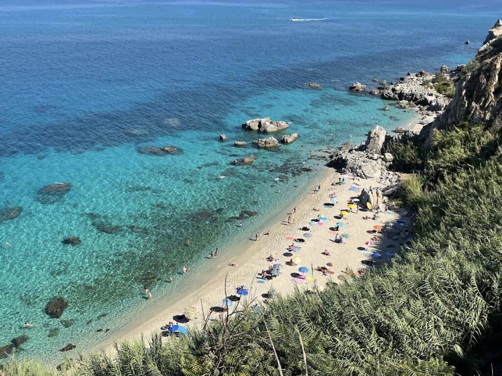 Beautiful Parghelia beach with cliffs, clear water, and colorful umbrellas.