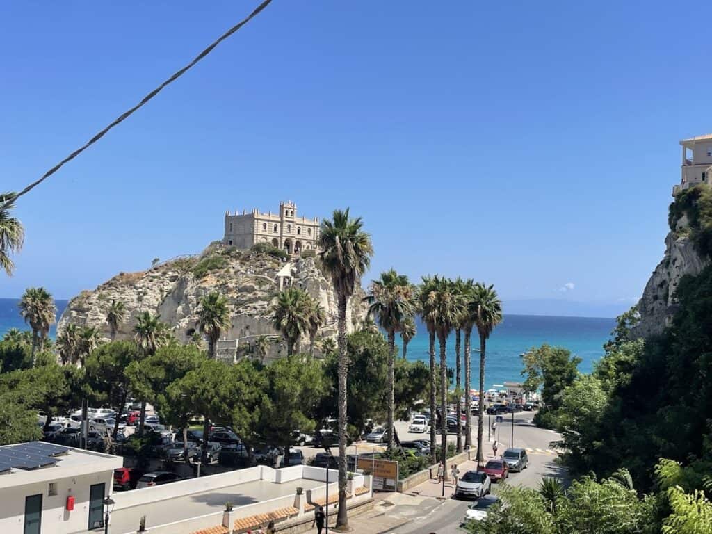 Beautiful coastal view of Tropea with historic castle and palm trees.