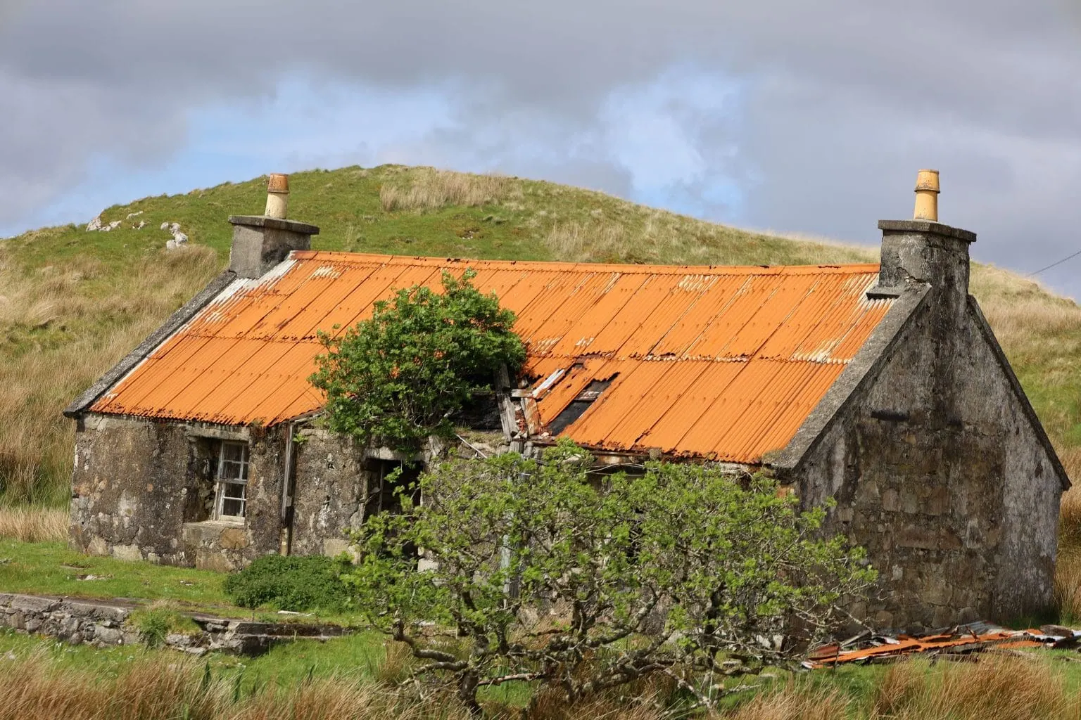 Old hillside rusty roof derelict and dilapidated old stone house, it has no door, tins sheeting missing from the roof lay on the ground.
