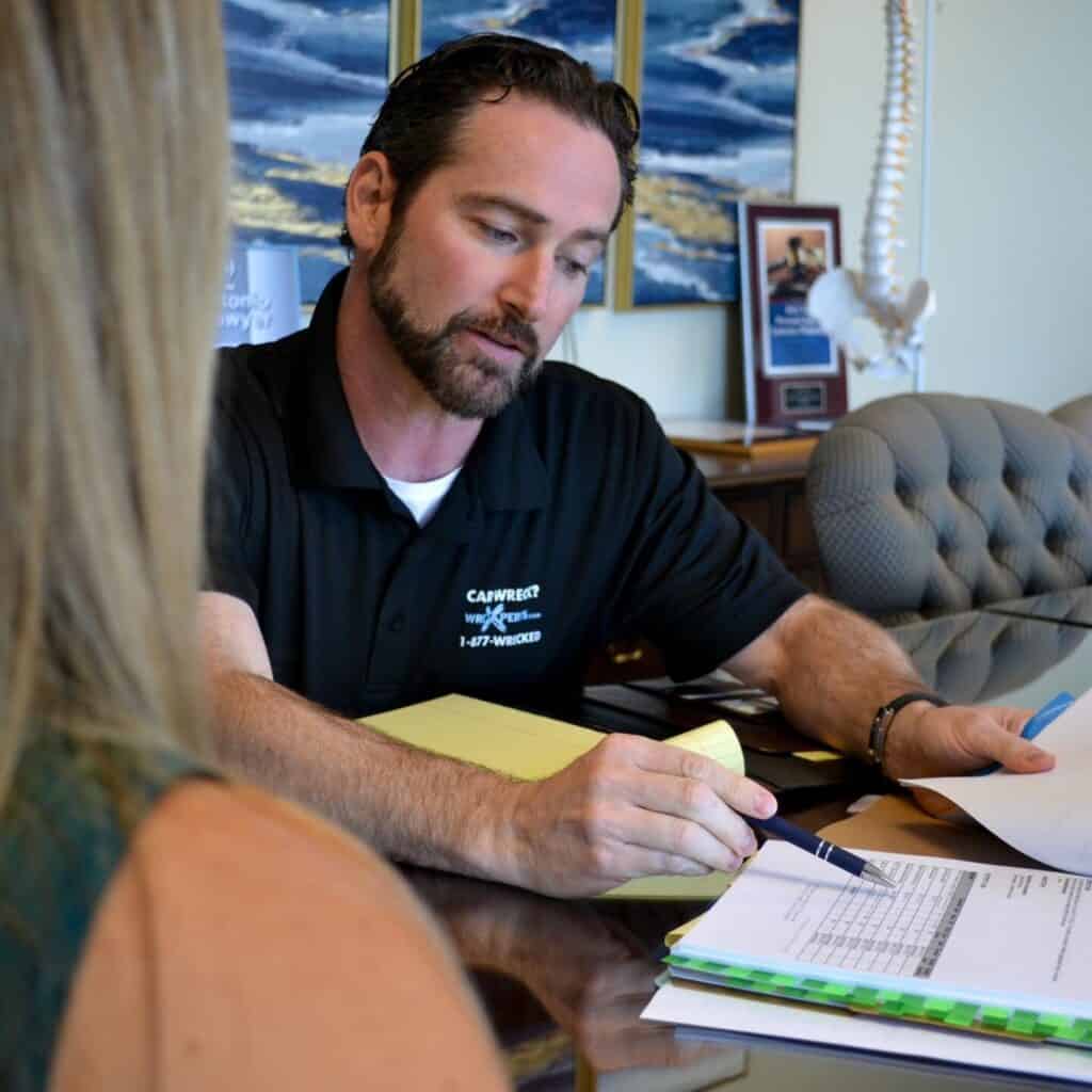 Man in a black polo shirt sitting at a desk, reviewing paperwork with a woman.