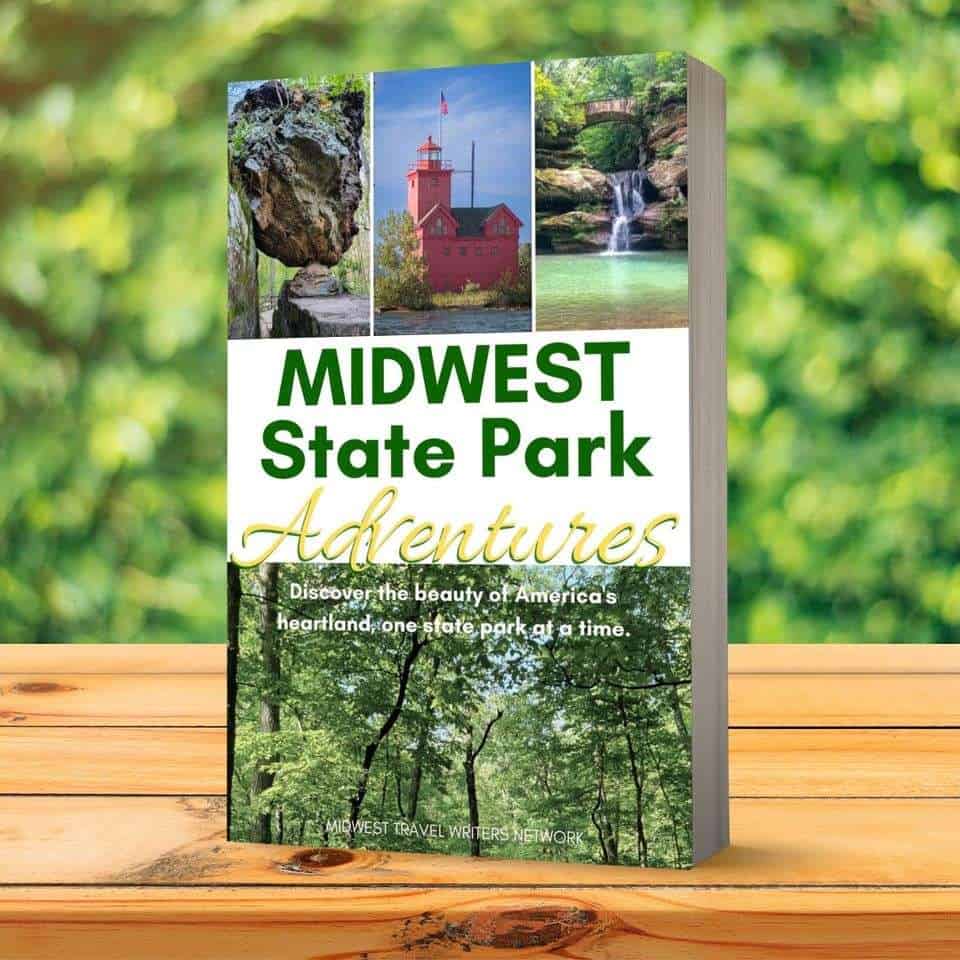 a book sits on a wooden table with greenery in the background. The book's title is Midwest State Park Adventures