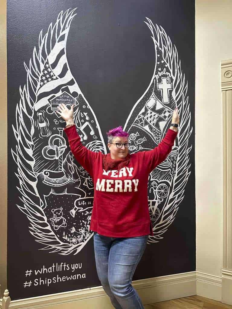 the pink-haired Hip Grandma poses in front of a pair of chalk designed wings