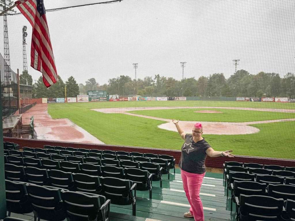 Pink-haired Hip Grandma stands overlooking a baseball field