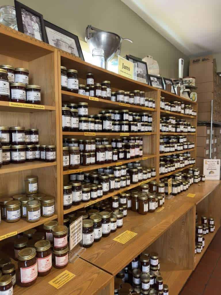 Shelves filled with jars of homemade jams and marmalades at an Amish country store, featuring flavors like strawberry, blackberry, and cherry.