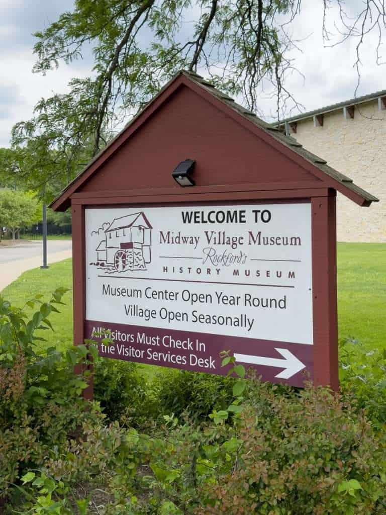 Entrance sign for Midway Village Museum in Rockford, Illinois, surrounded by greenery.