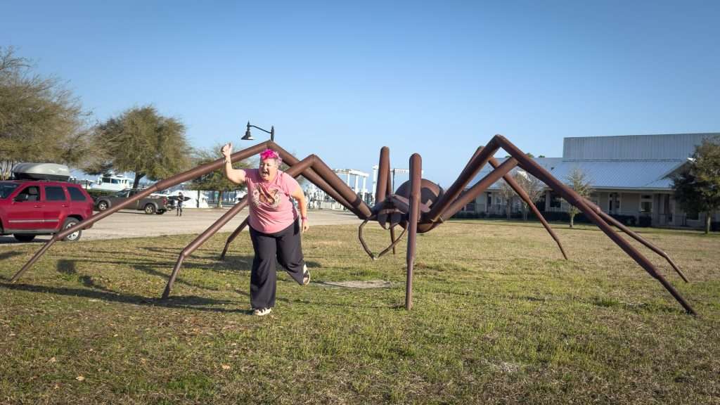 Woman with pink hair posing playfully beside the giant spider at Barber Marina in Elberta, Alabama