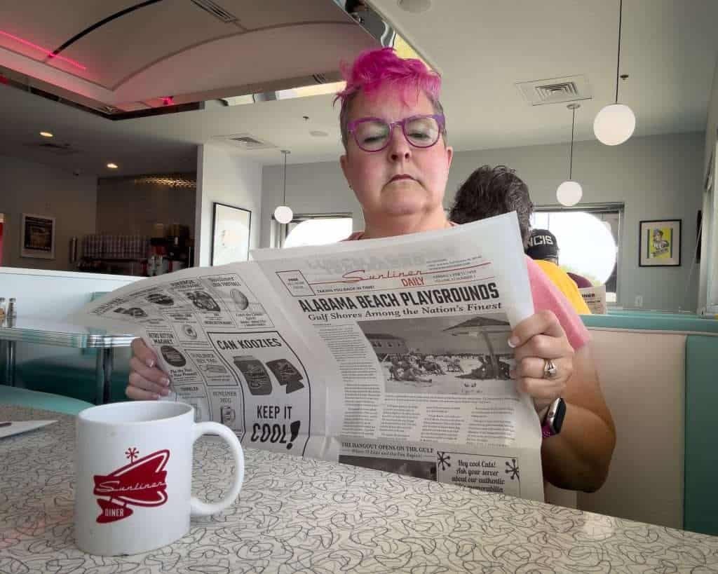 Woman with pink hair reading the Sunliner Daily newspaper inside Sunliner Diner in Gulf Shores, Alabama