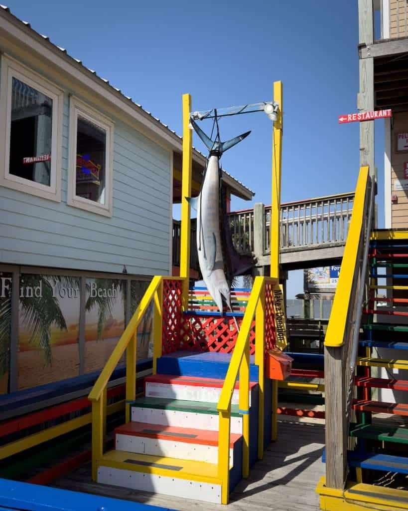 A large fish hangs from a yellow frame on a colorful staircase at a beachside location in Gulf Shores, Alabama.