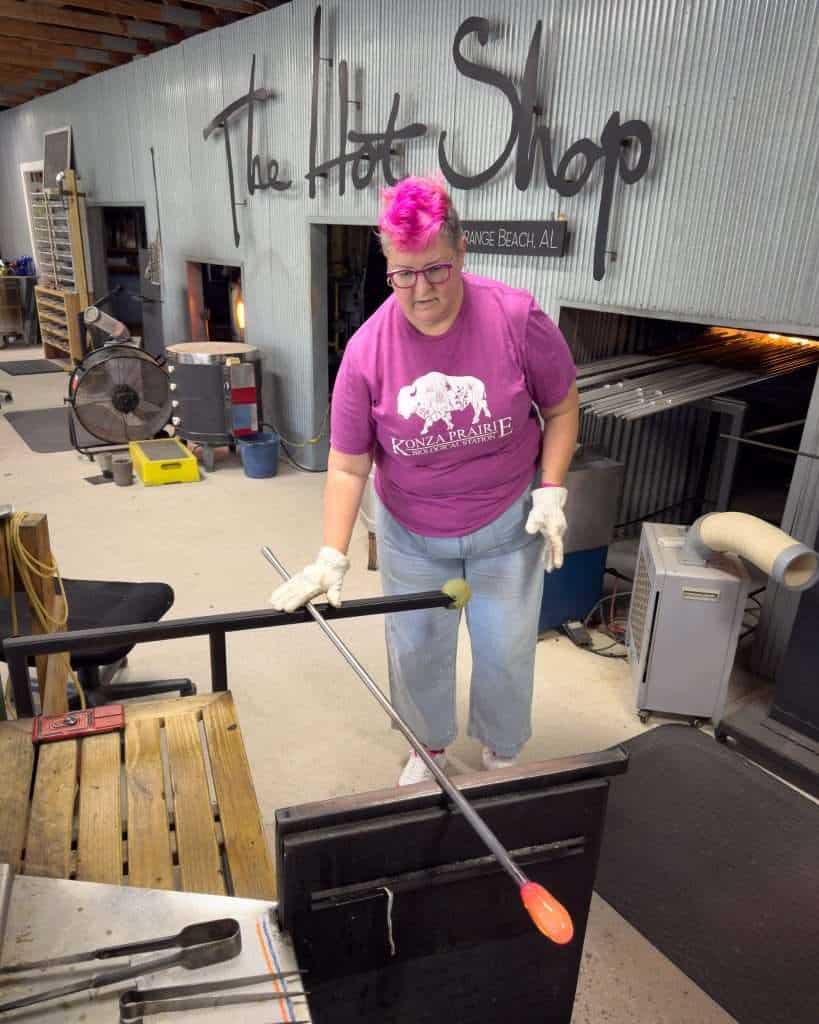 Woman shaping molten glass during a glassblowing demonstration at The Hot Shop in Orange Beach, Alabama