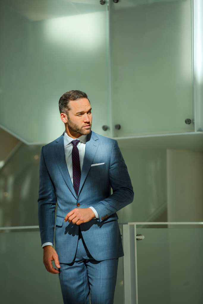 Business professional in a tailored blue suit, standing confidently indoors.