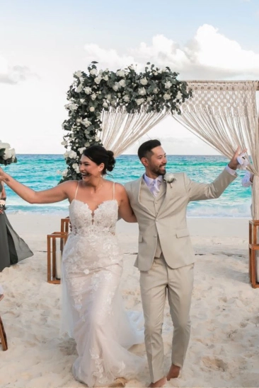 Wedding couple celebrating on the beach under floral arch.