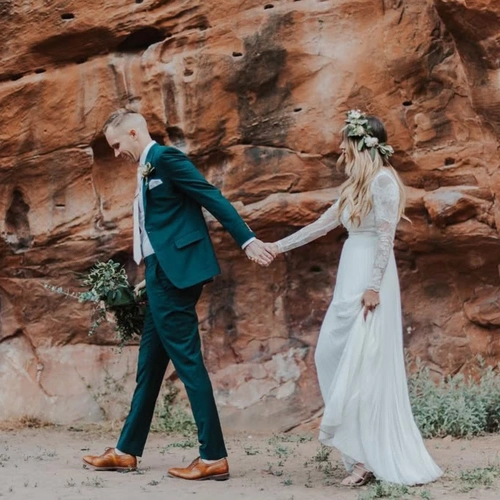Wedding couple holding hands outdoors against a red rock formation.