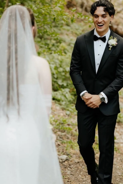 Groom in a classic black tuxedo with a white shirt and bow tie, smiling during his wedding vows outd.
